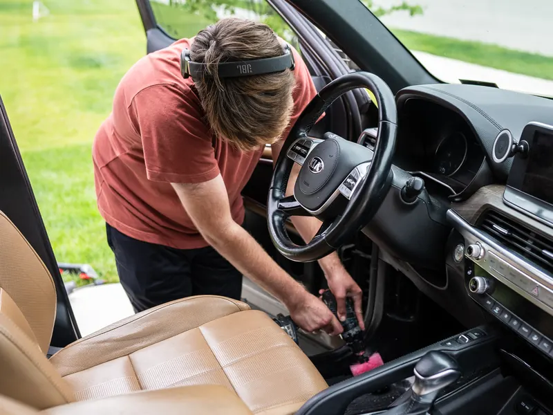 Levi kneeling at the driver door, scrubbing the footwell carpet