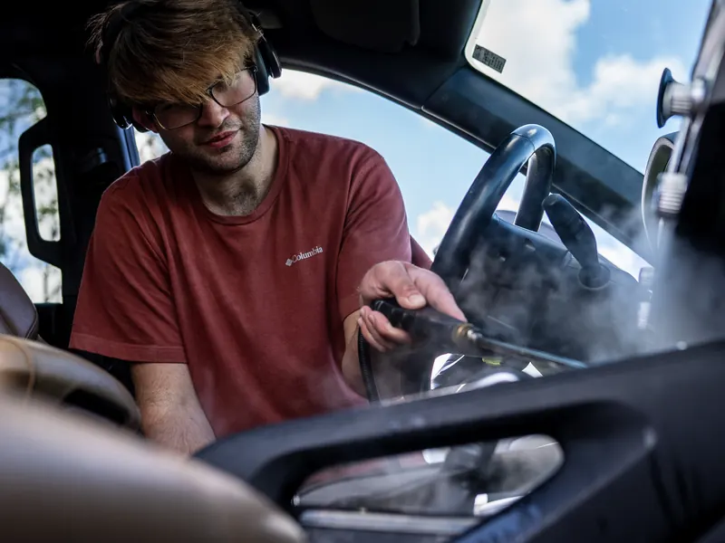 Levi Young leaning into the passenger side with a steam wand aimed at the center console