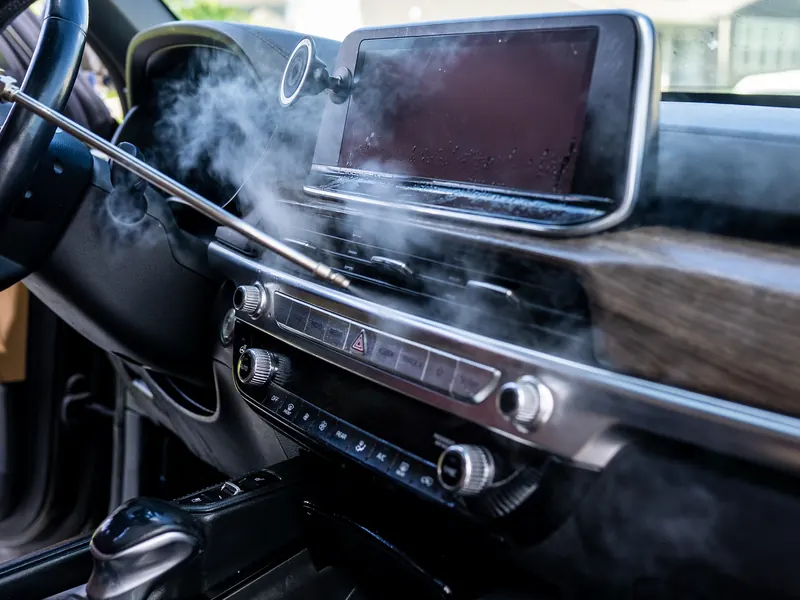 Steam wand clearing dust from the dashboard vents beside the touchscreen